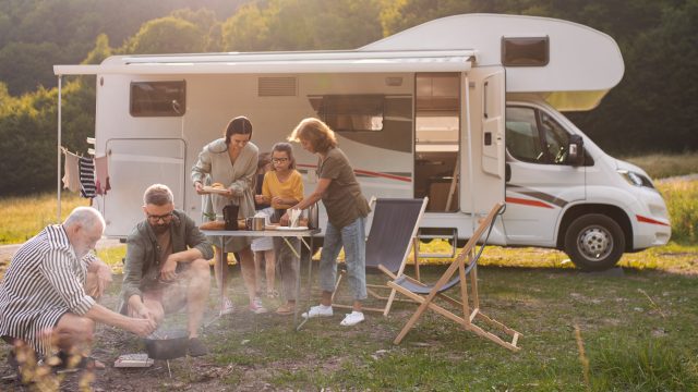 Familie som griller og setter frem mat foran en bobil.