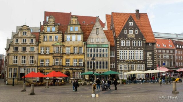 Et rolig stemningsfull bysentrumsbilde med mennesker og parasoller i forgrunn.