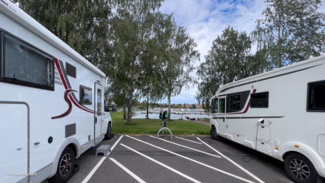 Dette bildet viser to hvite bobiler som er parkert side ved side på en asfaltert parkeringsplass. Bildet er tatt fra en vinkel som viser fronten og siden av begge bobiler, samt deler av området rundt dem.