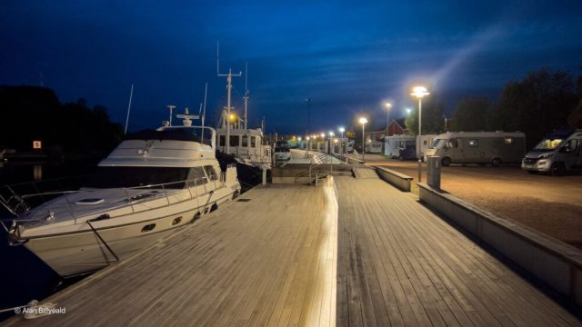 Nattlig bilde som viser en brygge med flere båter fortøyd. Bildet er tatt fra et høyt perspektiv, og vi ser ned på bryggen og båtene.
